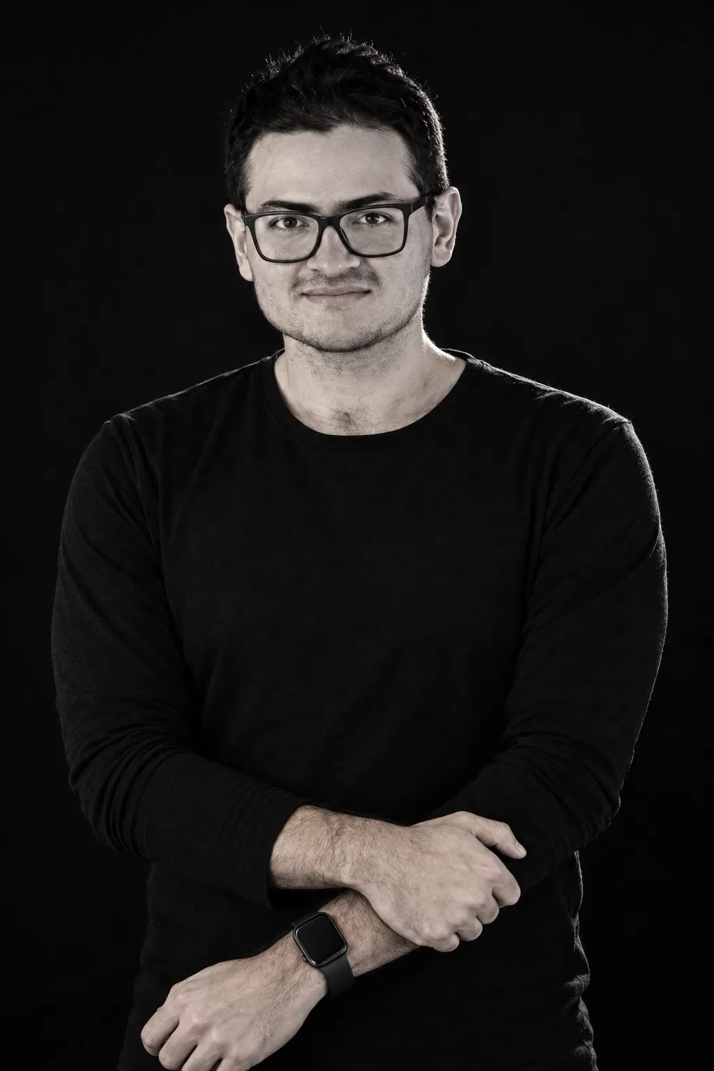 Portrait of José Rojas, arms crossed, wearing glasses and a black long-sleeve shirt